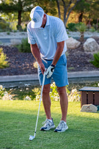 Man playing golf on a grassy course with trees in the background