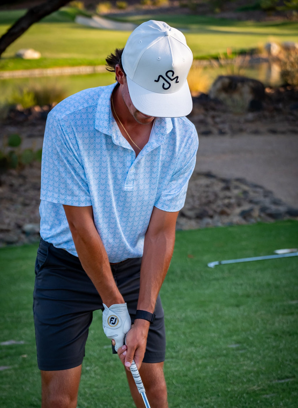 Young man on a golf course wearing a white cap and blue shirt, holding a golf club.