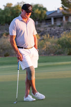 Man on a golf course holding a putter with a scenic background