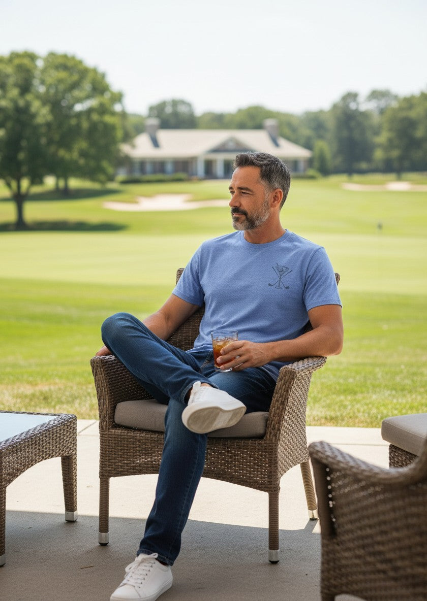 Man wearing a royal blue Scooter Martini tri-blend t-shirt with a golf-themed logo, sitting on a golf course patio.