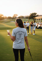 Woman wearing a heather white Scooter Martini tri-blend t-shirt with a golf-themed martini logo on a golf course.